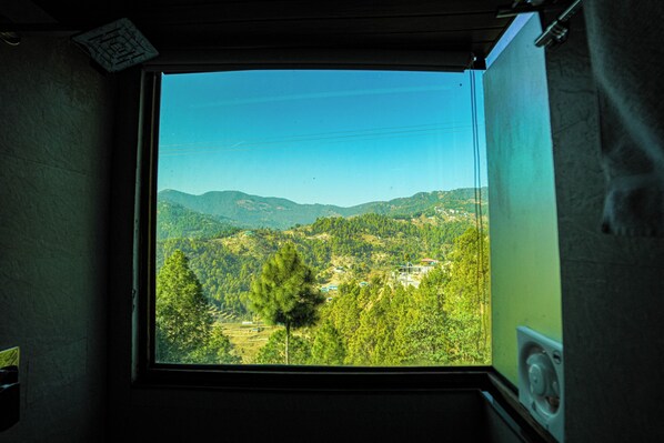 A window with a view of a mountainous landscape, including trees and buildings.