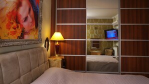 A hotel room with a large bed, a bedside table with a lamp, a television on a stand, and a sliding closet door. - Violeta s Seaview Apartment in Piraeus (Piraeus)