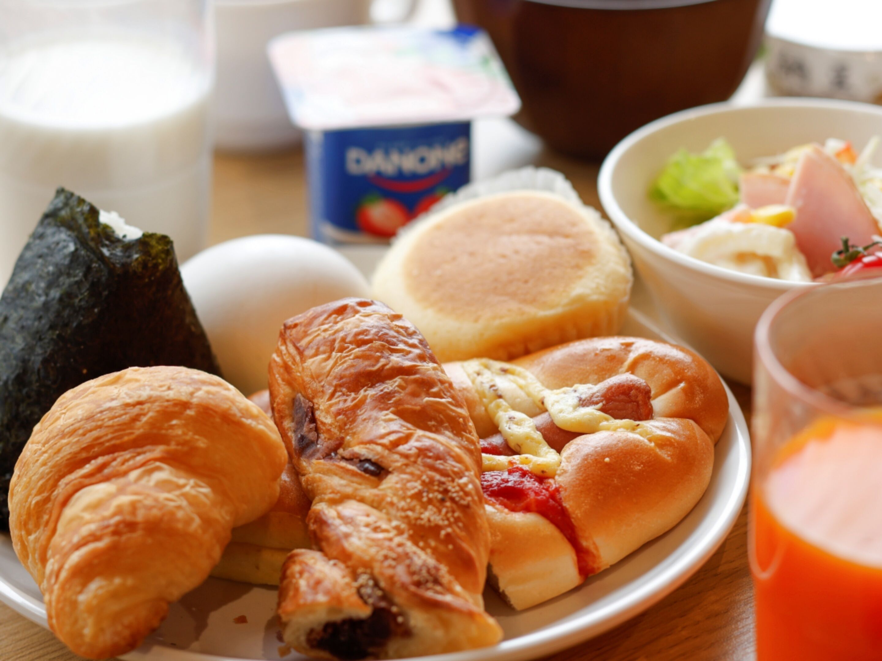 A plate with croissants, a ham sandwich, and a bowl of salad.