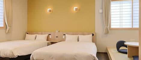 A hotel room with two beds, a small table, and a chair.