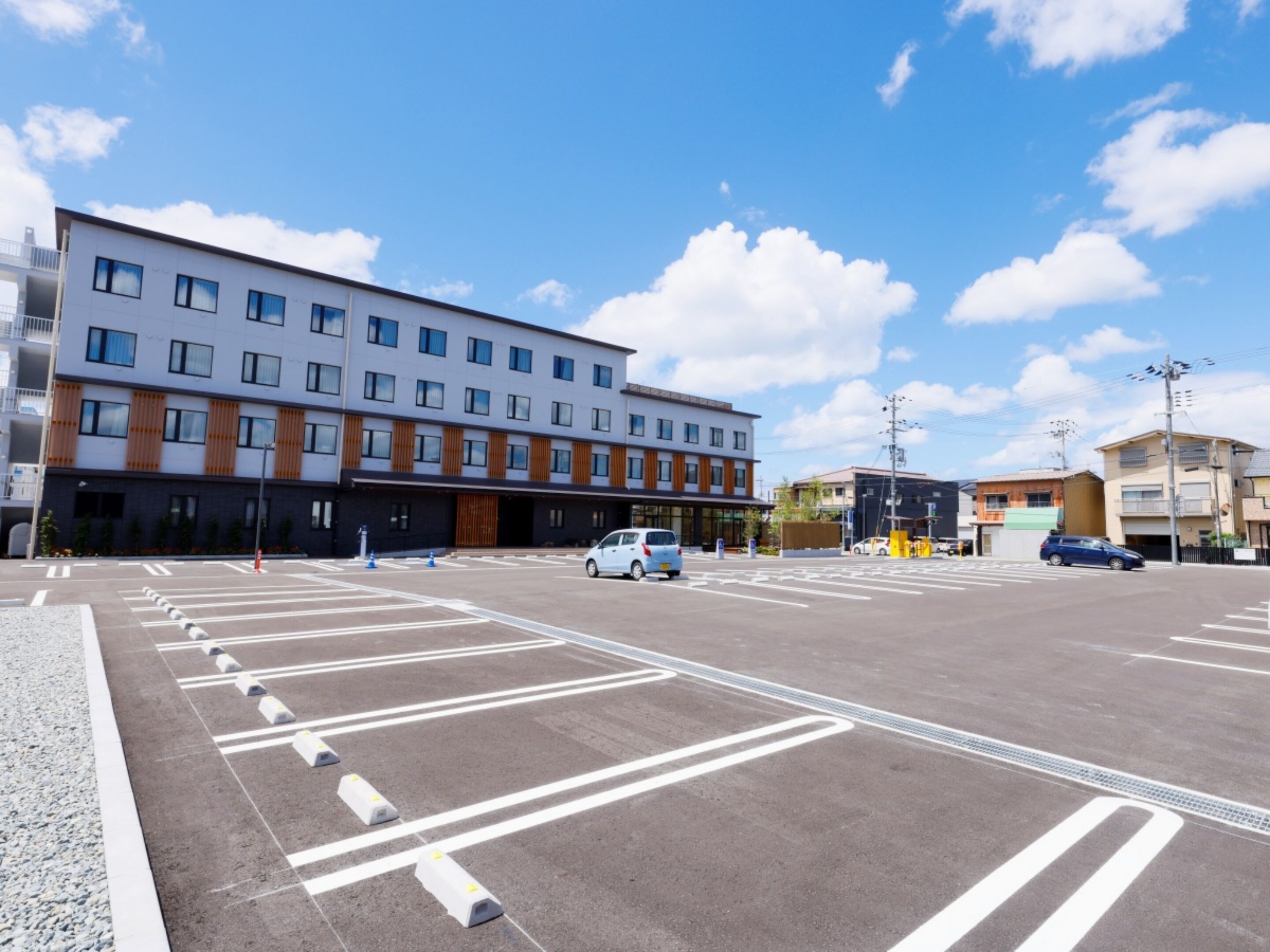 A parking lot with marked lanes and bollards, a modern building with multiple floors and large windows, and a clear blue sky with scattered clouds.