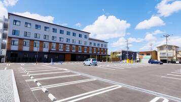 A parking lot with marked lanes and bollards, a modern building with multiple floors and large windows, and a clear blue sky with scattered clouds.