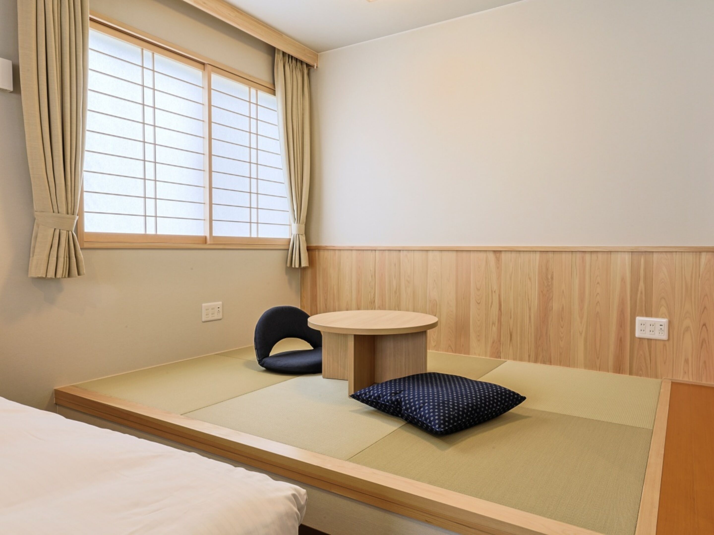 A room with tatami flooring, a futon bed, a small round table, and a chair.