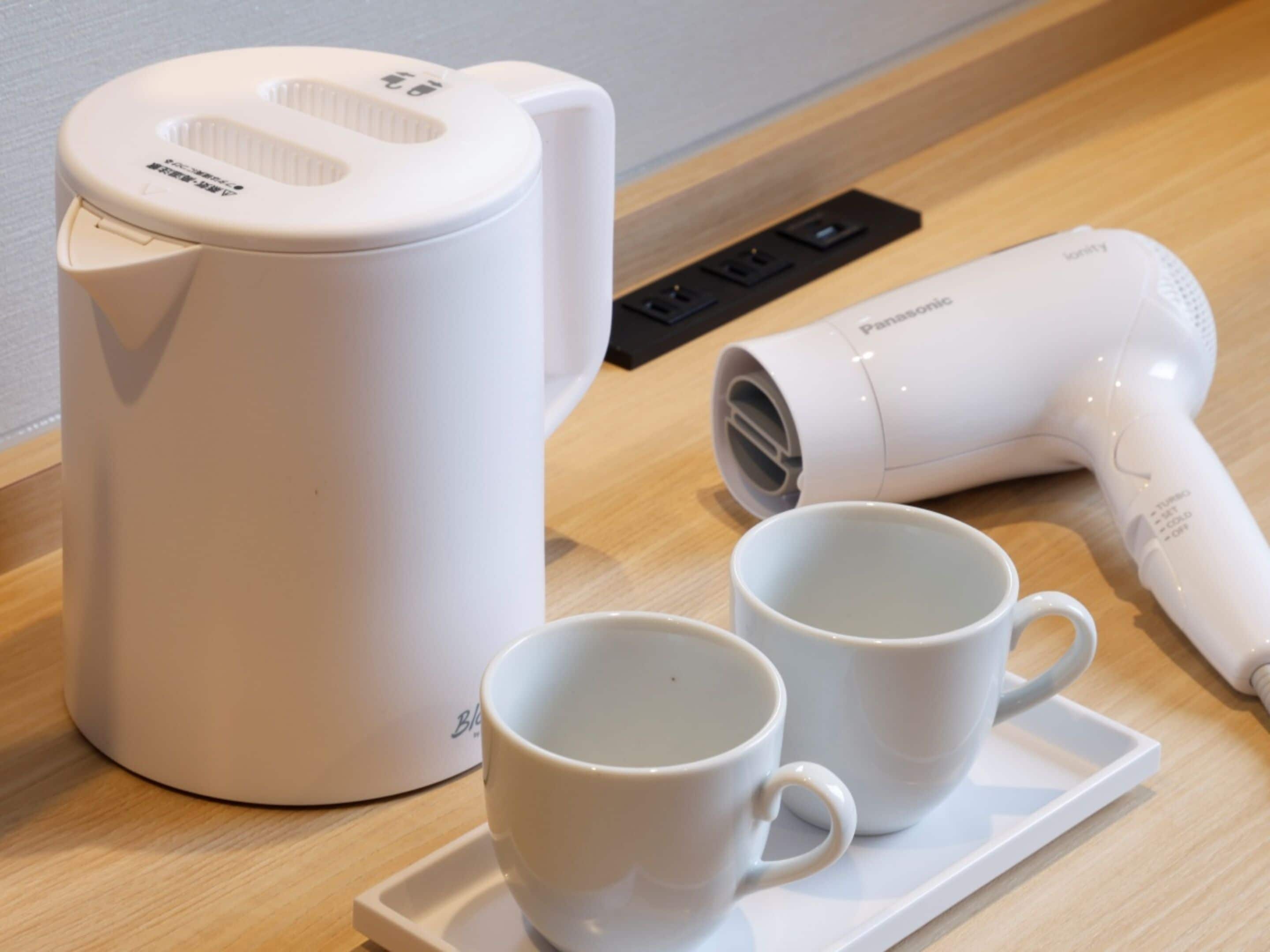 A white coffee maker, a hair dryer, and two white cups on a tray.