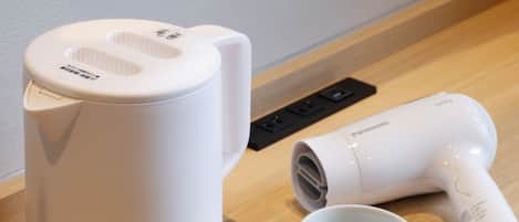 A white coffee maker, a hair dryer, and two white cups on a tray.