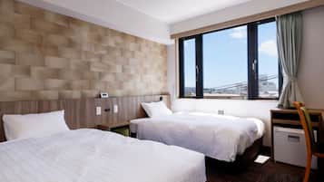 A hotel room with two beds, a wooden headboard, a window with a view, and a desk with a chair.