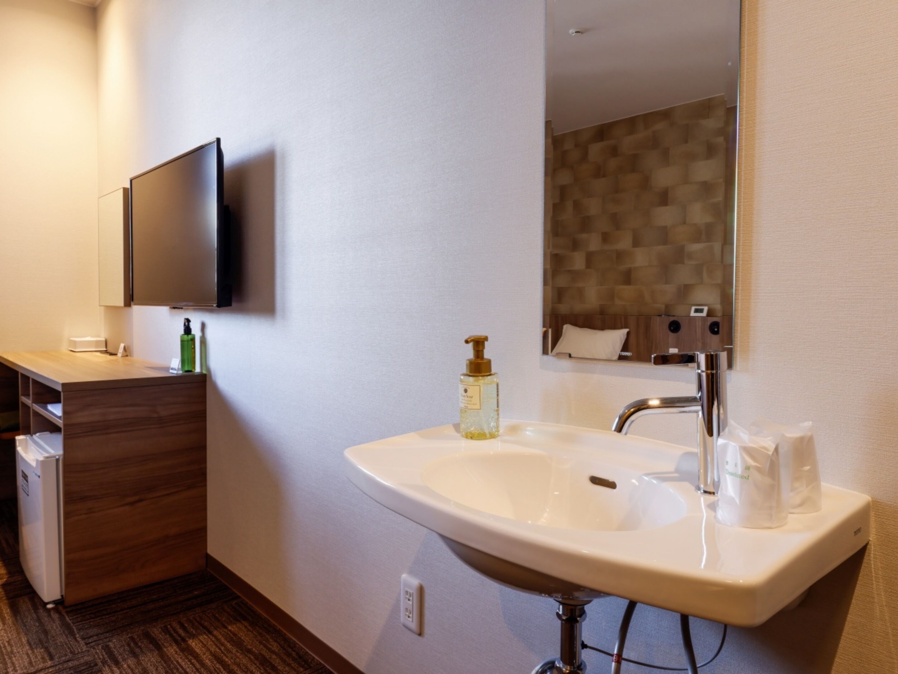 A modern bathroom with a large sink, a mirror, a television mounted on the wall, and a wooden vanity.