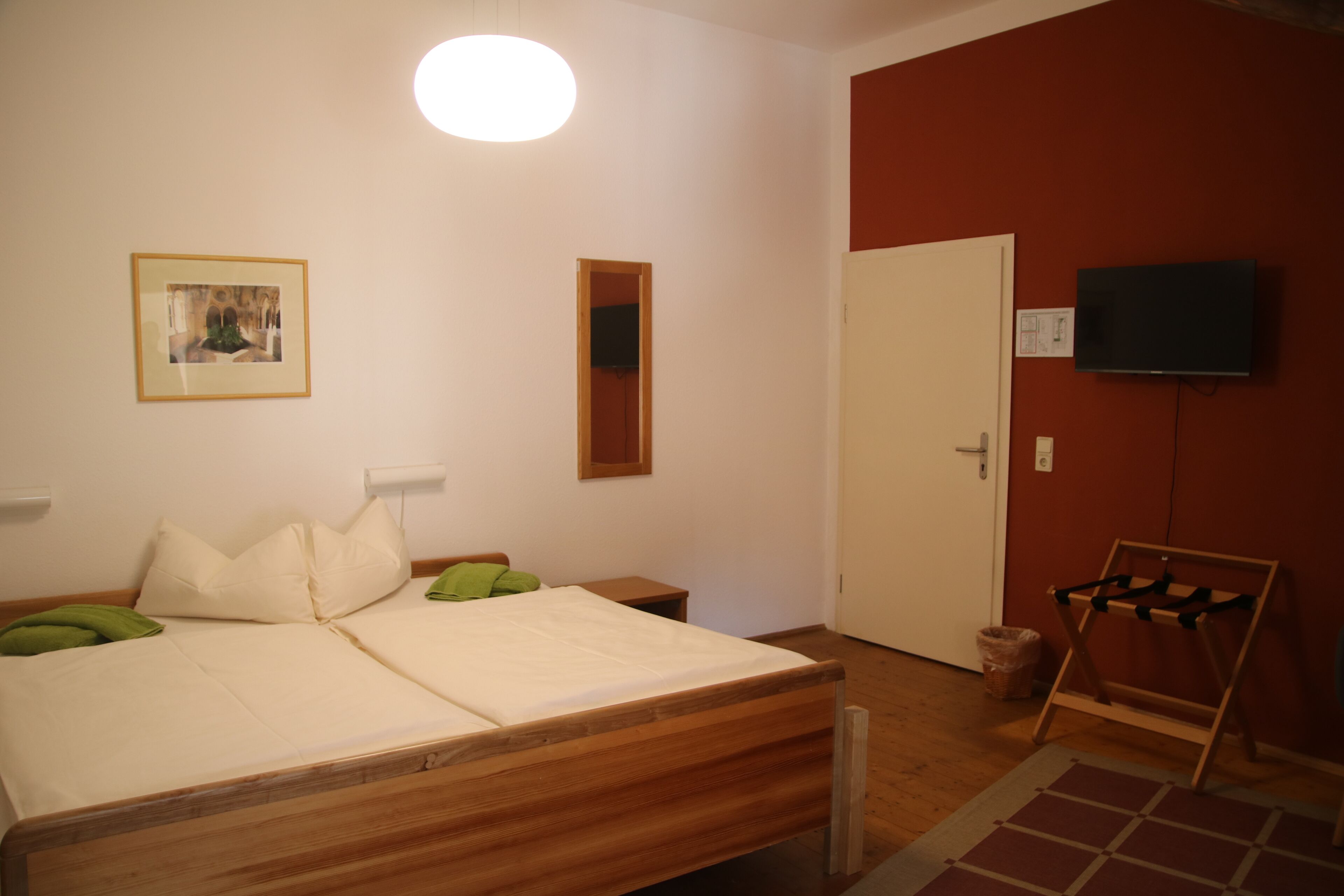 Um quarto com uma cama de madeira, uma televisão fixada na parede e uma porta.