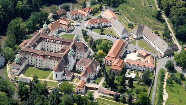An aerial view of a large, historic building complex with multiple wings and domed structures, surrounded by lush greenery and a river. - Gästehäuser St Marienthal (Ostritz)