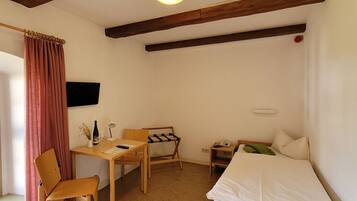 A small, cozy room with a wooden bed, a desk with a chair, a small table, and a hanging coat rack.