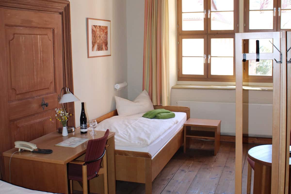 Una habitación con una cama de madera, un escritorio con lámpara, una silla y una ventana con cortinas.