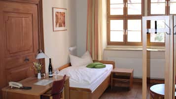 A room with a wooden bed, a desk with a lamp, a chair, and a window with curtains.