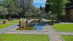 A garden with a pond, potted plants, and a brick wall. - Gästehäuser St Marienthal (Ostritz)