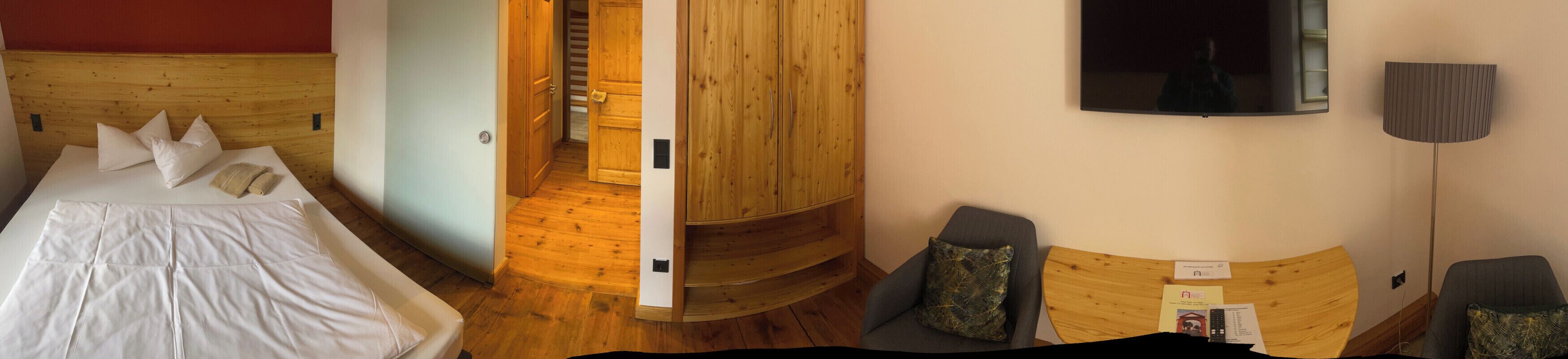 Una habitación de hotel con cama de madera con cabecera, televisor montado en la pared, una escalera de madera y un área de descanso con una mesa.