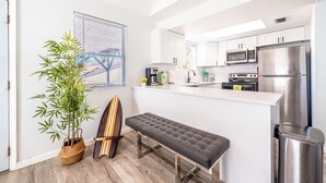 Une cuisine moderne avec des meubles blancs, des appareils en acier inoxydable, un banc et un pot de bambou.