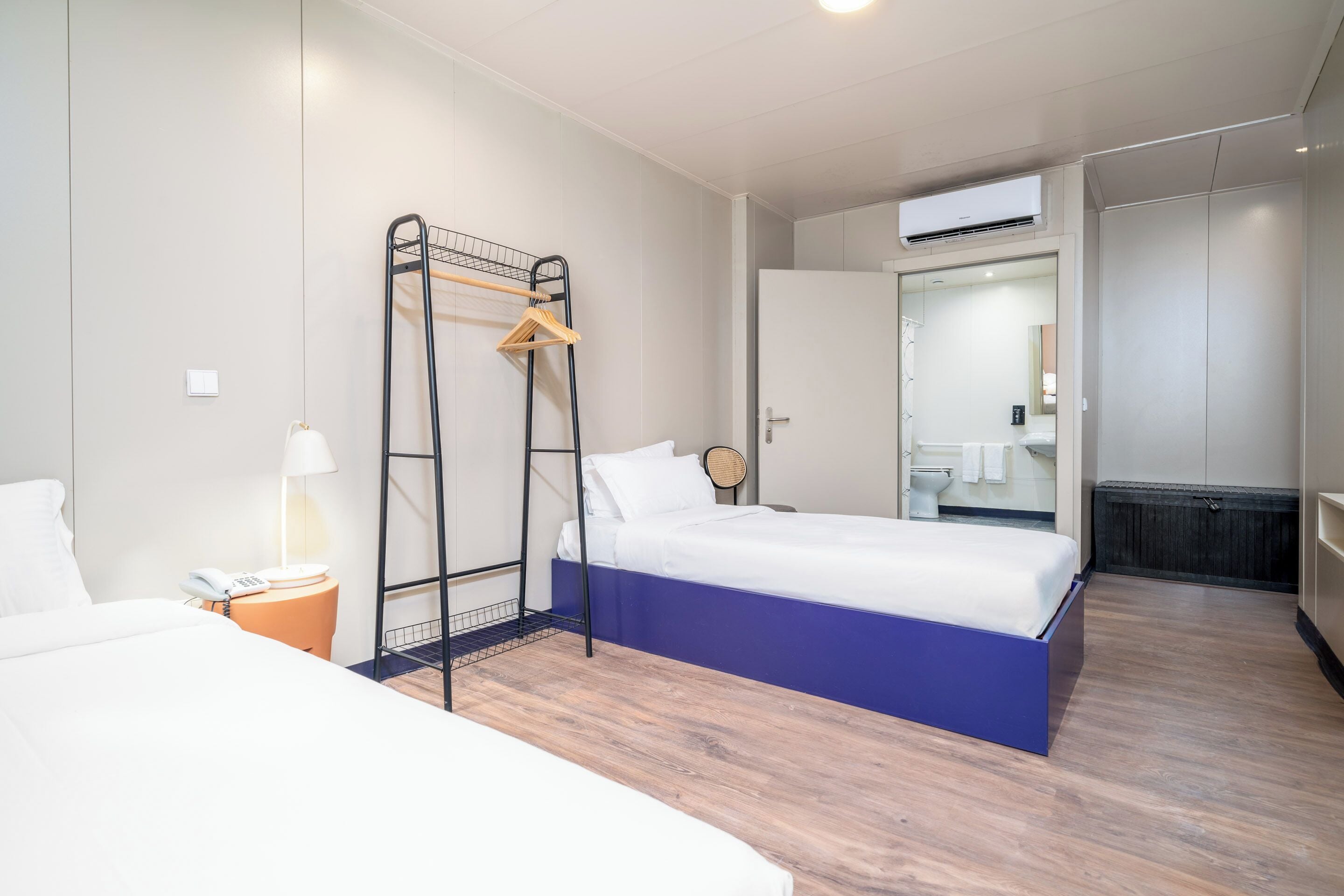 Une chambre d’hôtel comprenant un lit, une table de chevet avec une lampe, une armoire et un appareil de climatisation.