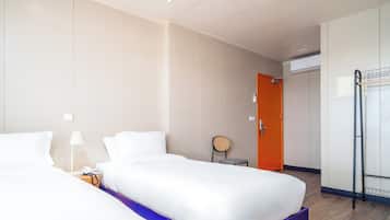 A hotel room with two beds, a small table with a lamp, a chair, and a wardrobe.