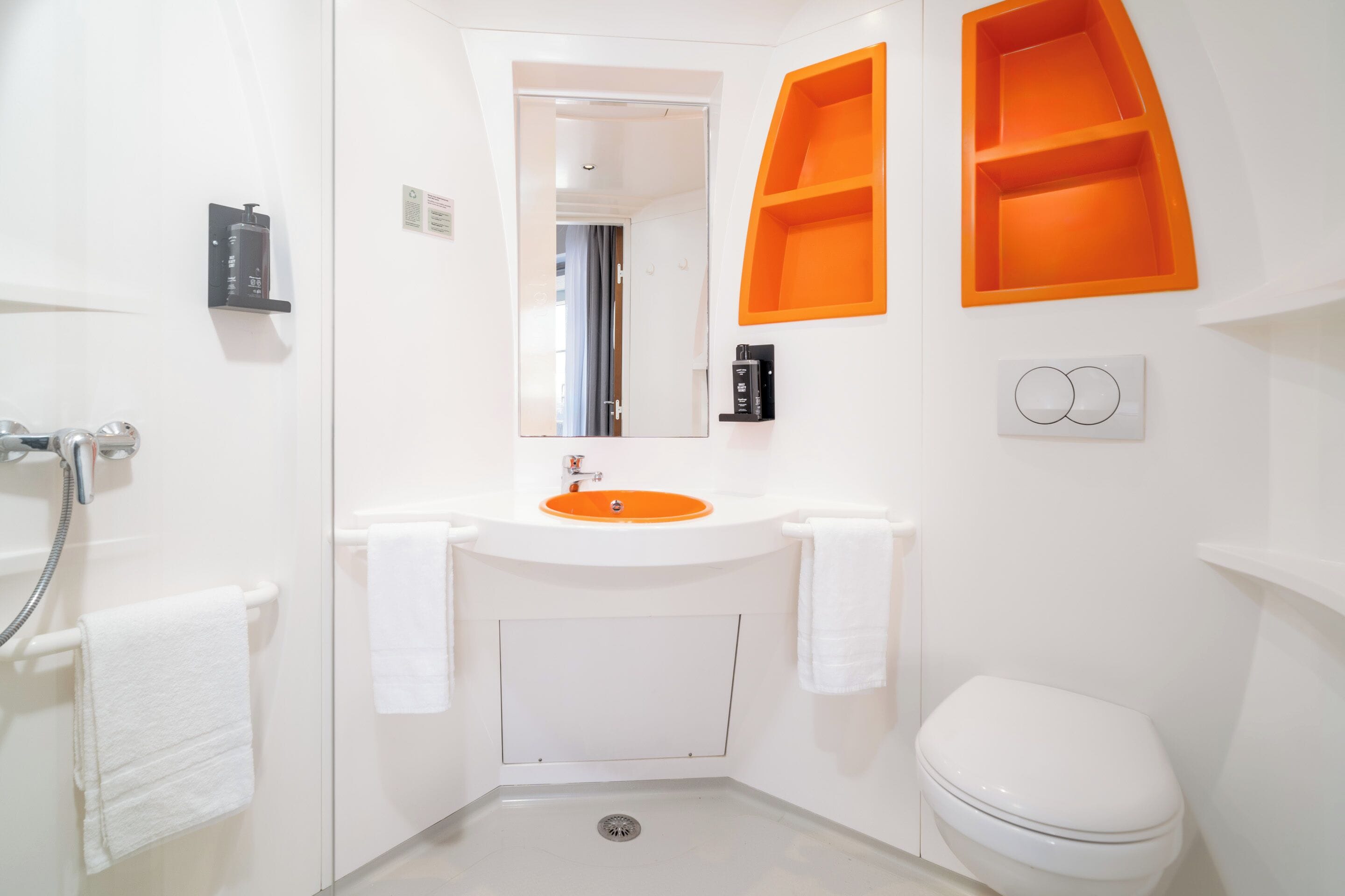 A bathroom with a white sink, a white toilet, and an orange shelf unit.