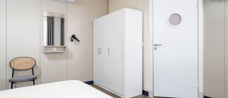 A bedroom with a bed, a wardrobe, a chair, a mirror, and an air conditioning unit.