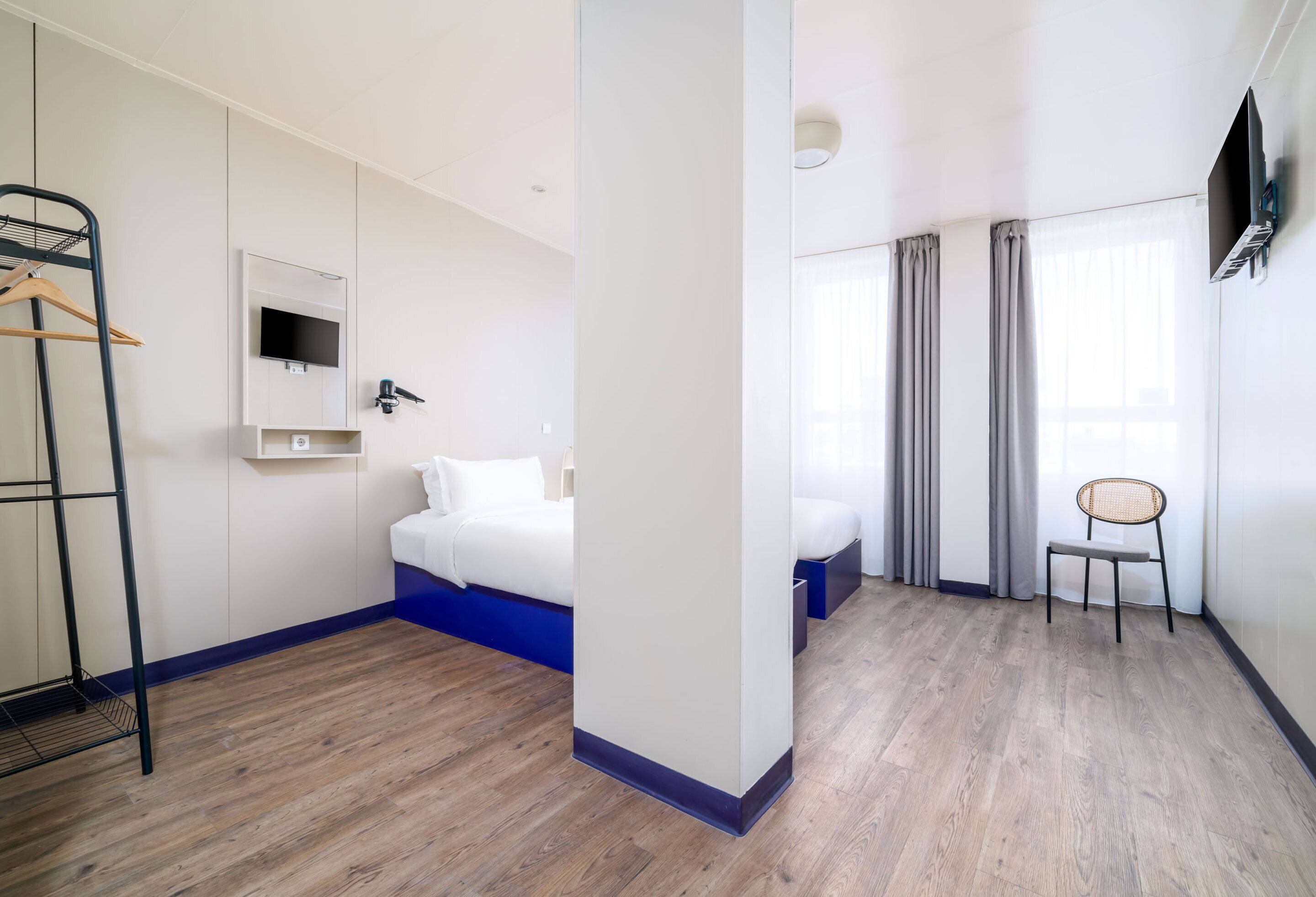 A hotel room with a bed, a chair, a TV, and a wardrobe.
