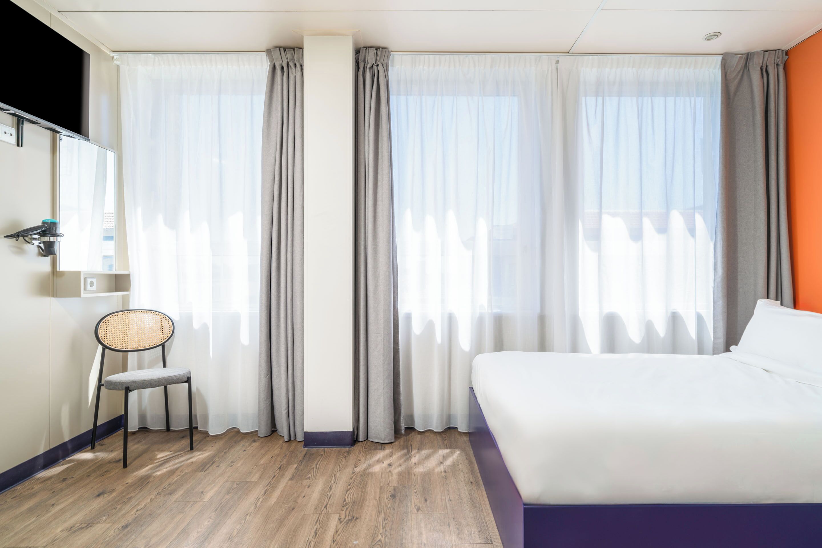 Une chambre d’hôtel avec un lit, une chaise et des rideaux.