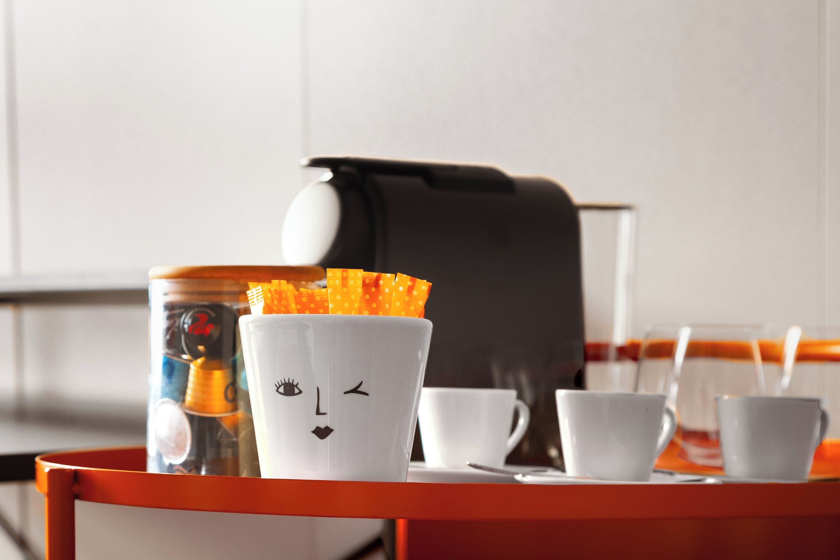 A tray with a coffee maker, a cup with a face, and several white cups.