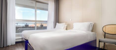 A hotel room with two beds, a large window, a chair, and a view of the city.