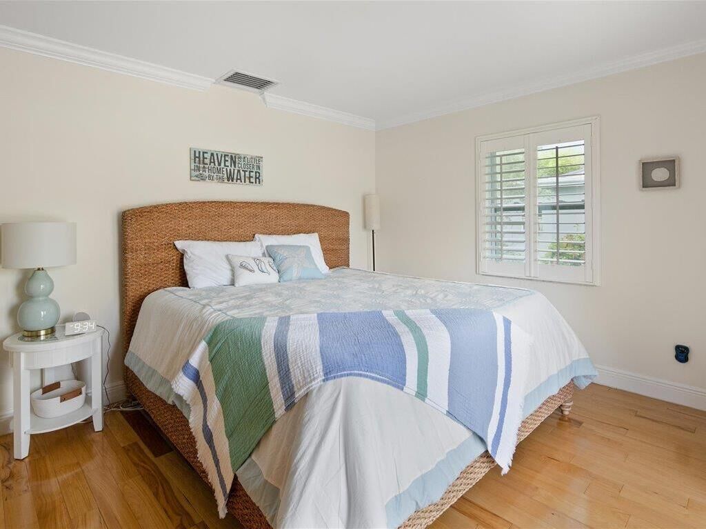 Une chambre à coucher comprenant un lit, une table de chevet, une lampe, une fenêtre avec des stores et un tableau décoratif au mur.