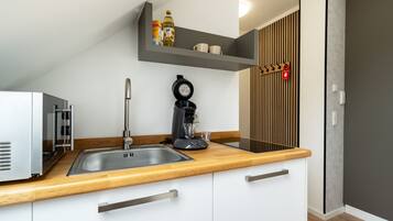 Une cuisine moderne équipée d’un four encastré, d’une machine à café et d’une étagère contenant les ustensiles de cuisine essentiels.