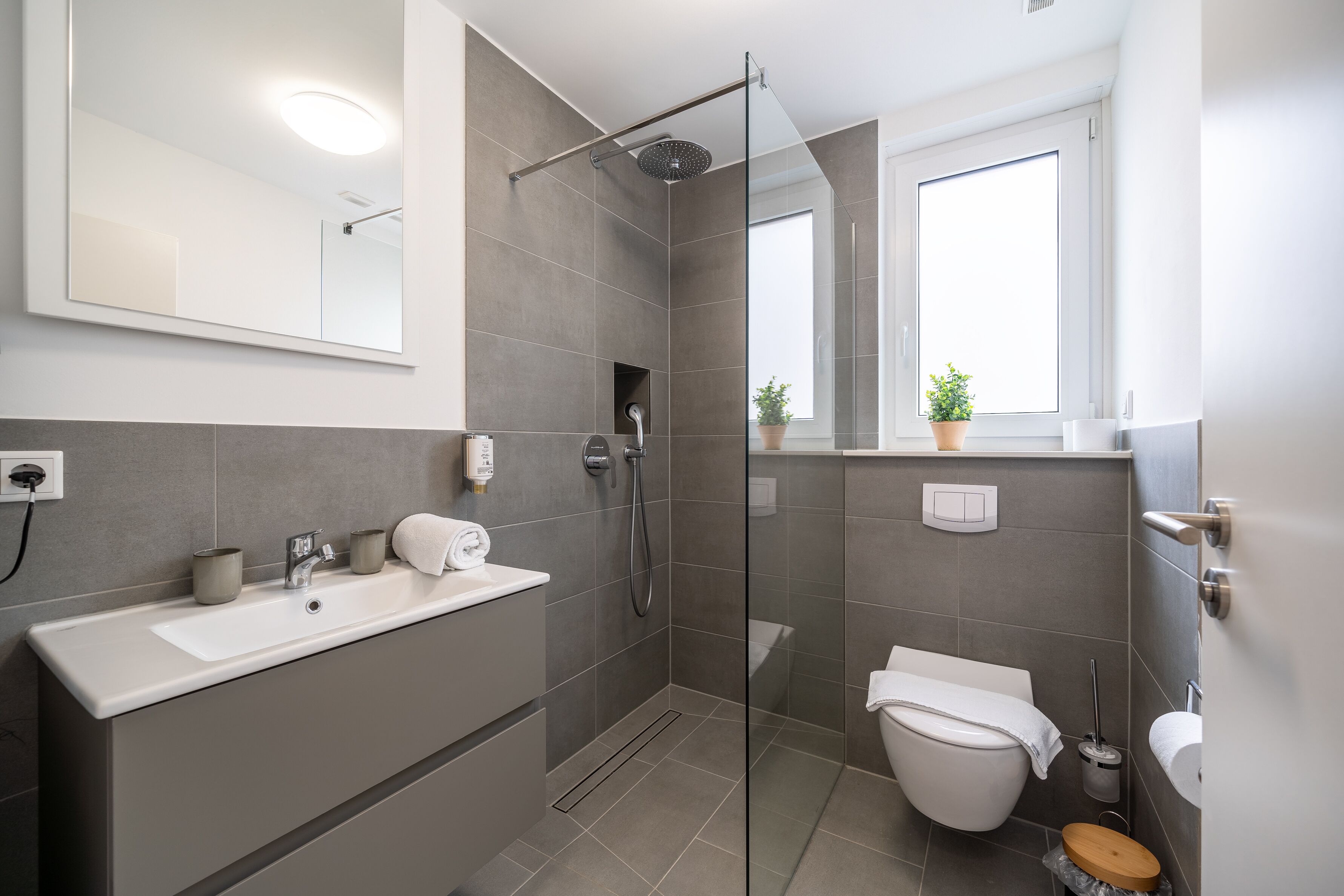 Un baño moderno con ducha envuelta en vidrio, un lavamanos blanco y un inodoro.