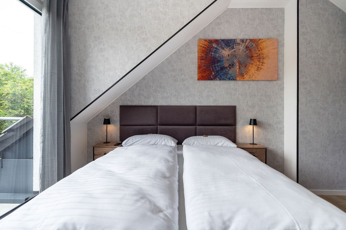 A modern bedroom with two beds, a large window, and a unique wall art piece.