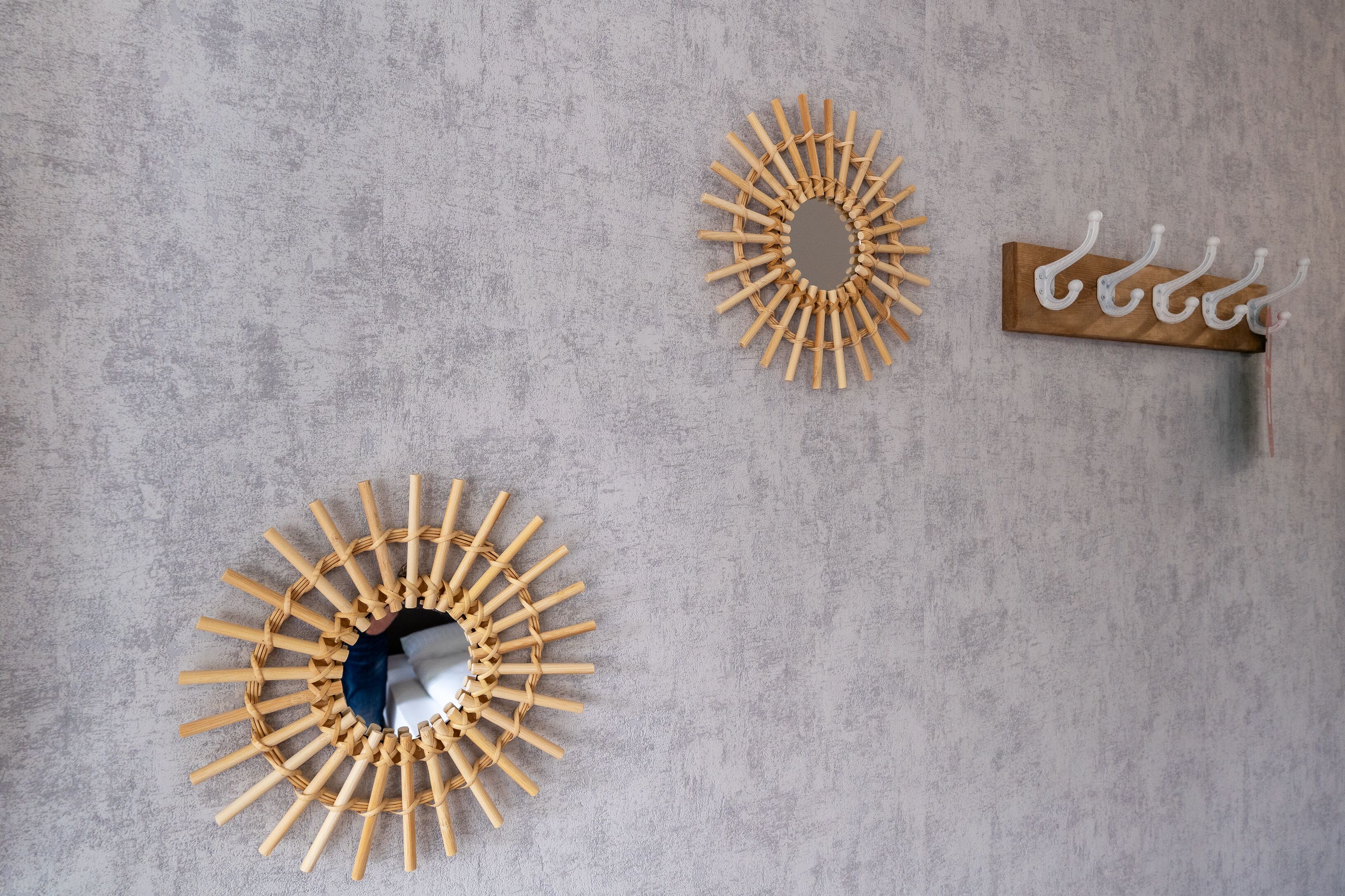 A wall with three wall-mounted items: a circular mirror with a wooden frame, a circular mirror with a wooden frame, and a wooden wall-mounted rack with hooks.