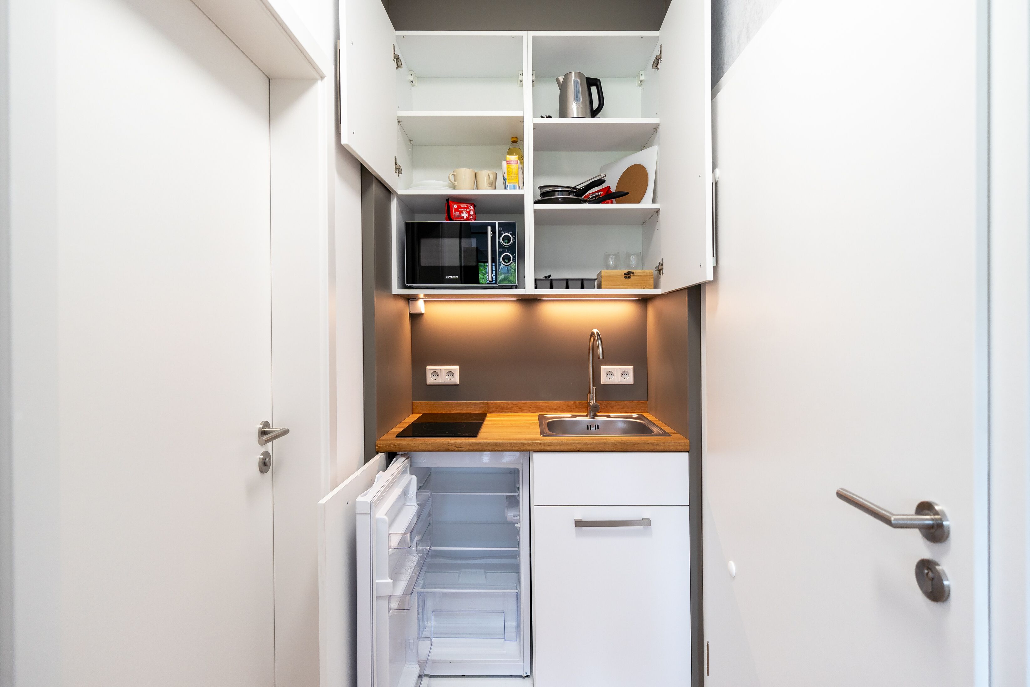A compact kitchen with a built-in microwave, a sink, and a small refrigerator.