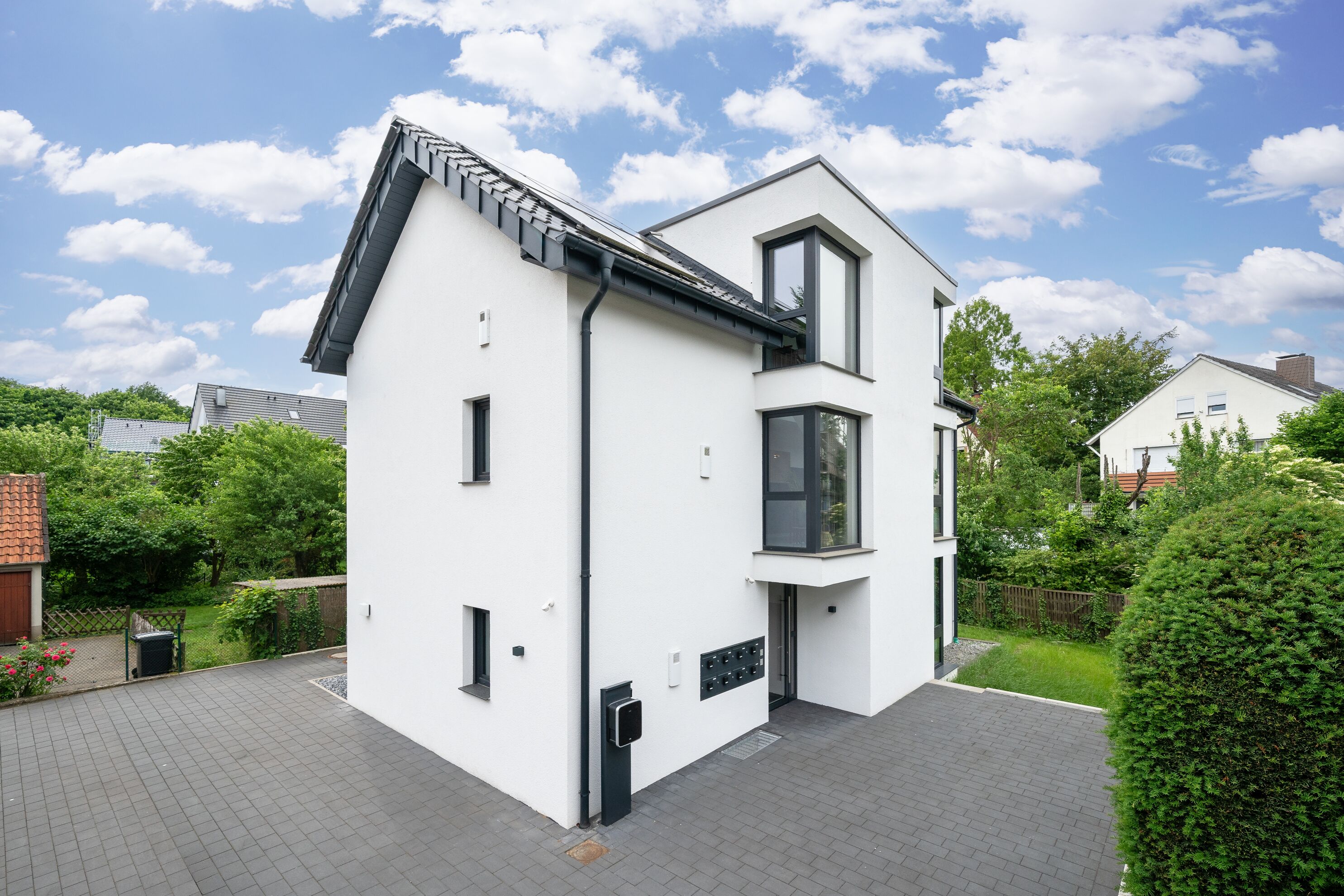 A modern two-story house with a white exterior, black roof, and large windows.