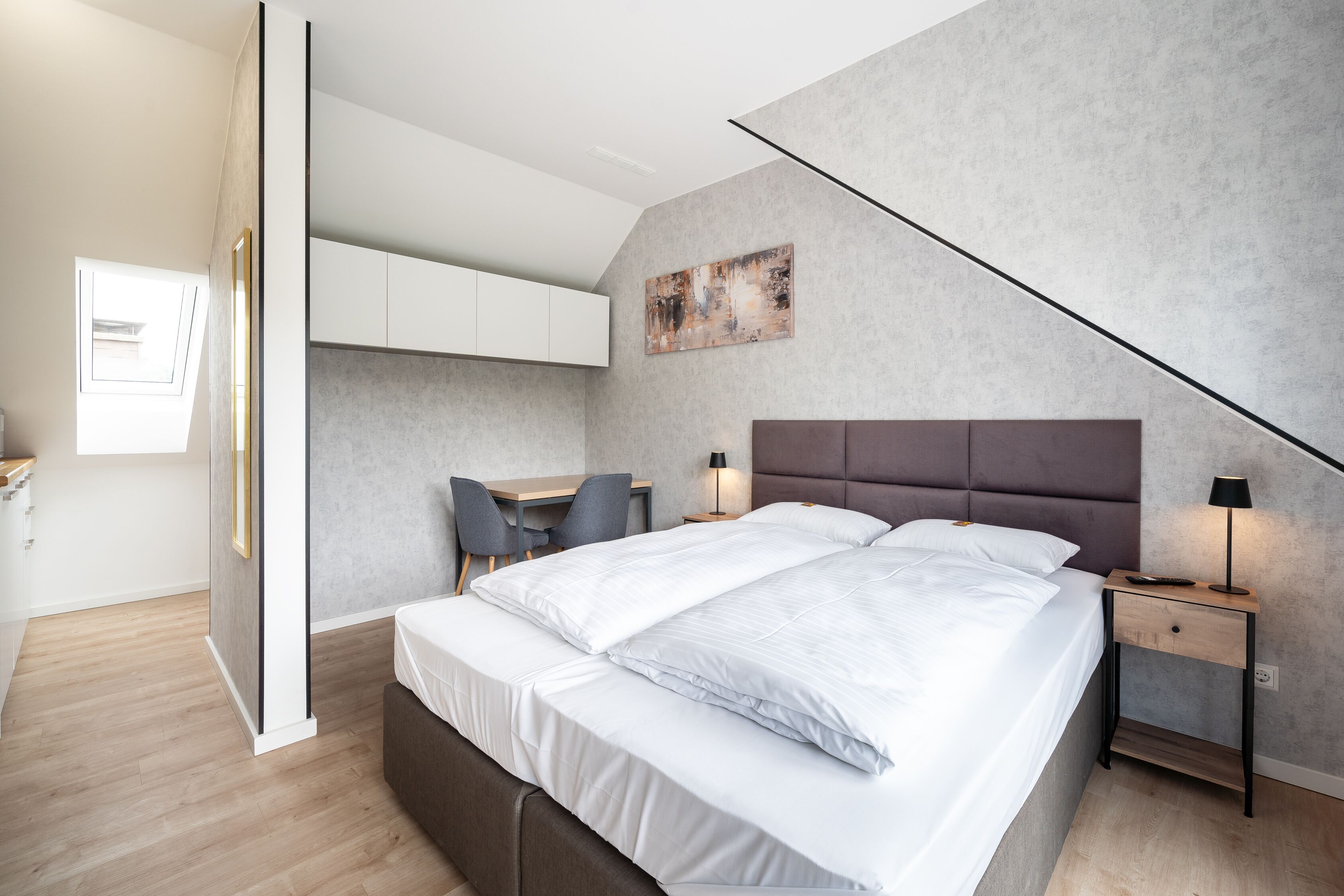 A modern bedroom with a large bed, bedside tables, a desk, and a chair.