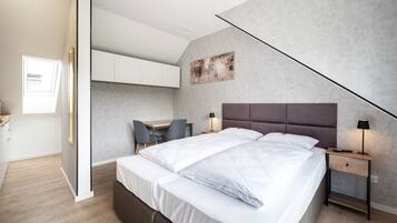 A modern bedroom with a large bed, bedside tables, a desk, and a chair.