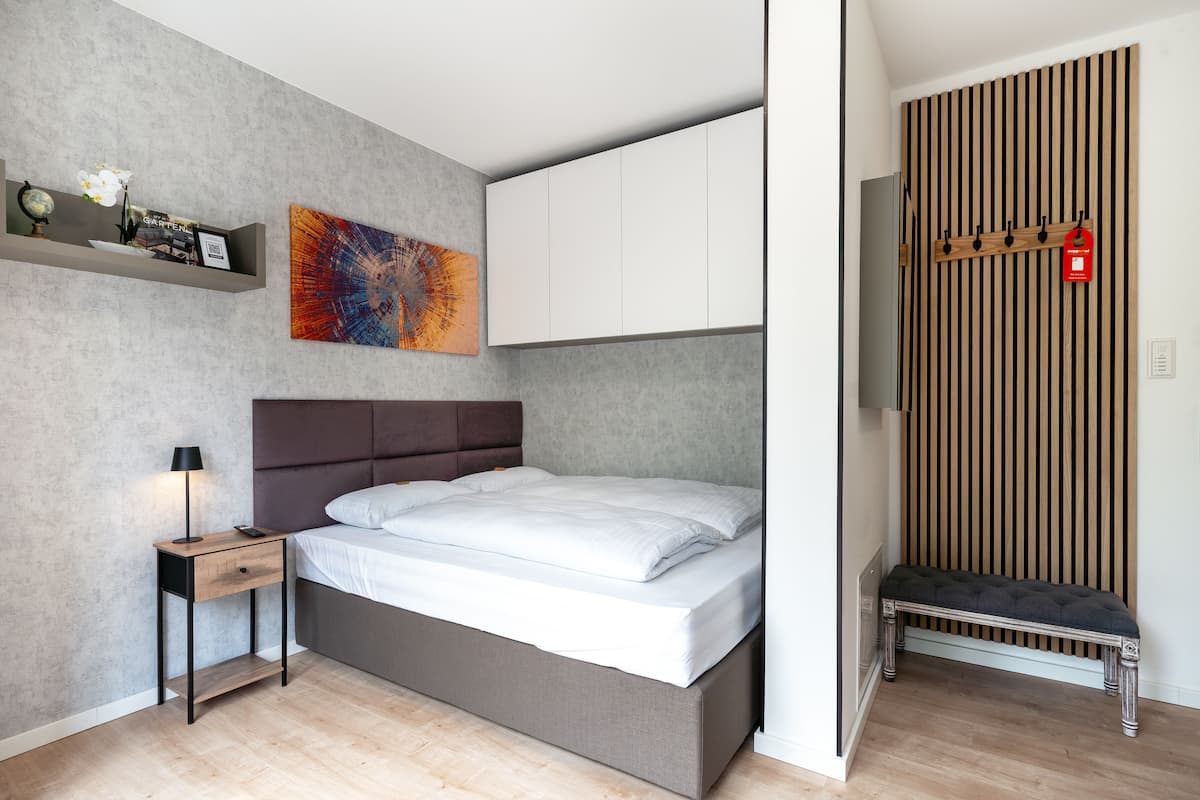 A modern bedroom with a bed, bedside table, and a wall-mounted shelf with decorative items.