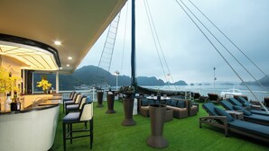 A deck with green artificial turf, lounge chairs, and a bar area with bottles. -  Le Journey Luxury Cruise (Tuan Chau)