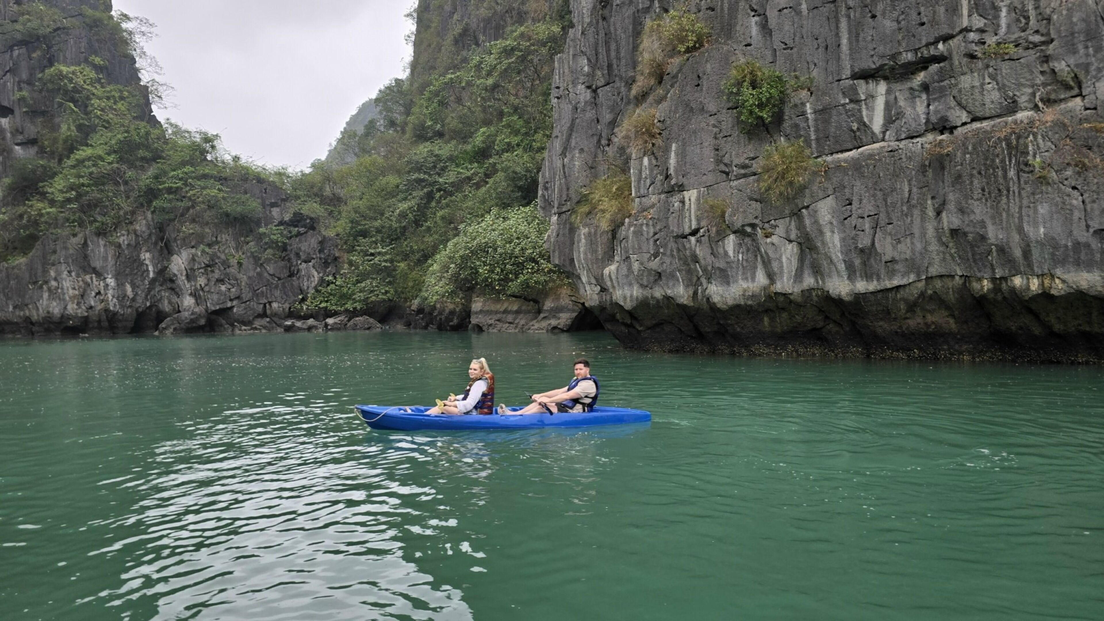Una pareja en kayak azul sobre aguas tranquilas, rodeada de imponentes acantilados rocosos.
