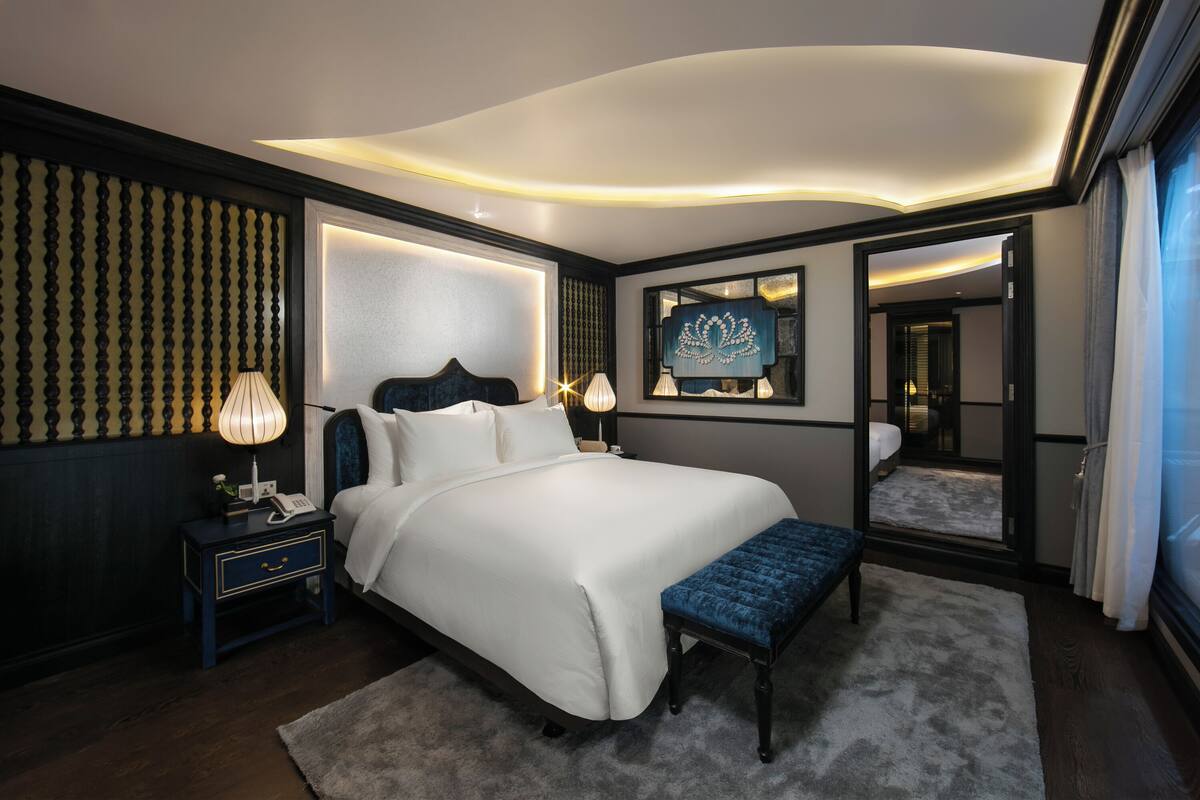 Une chambre d’hôtel moderne avec un grand lit, des lampes de chevet, une table de chevet, un banc et un miroir.