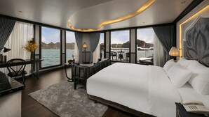 A modern hotel room with a large bed, a desk, and a view of the water. -  Le Journey Luxury Cruise (Tuan Chau)