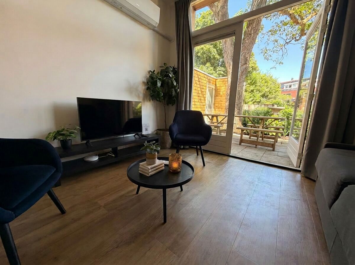 Modern living area with smart TV, comfortable seating, and direct access to a private terrace surrounded by greenery.