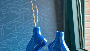 A blue vase with a unique shape on a black surface near a window with a brick wall.