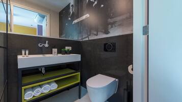 A compact bathroom with a white sink, black and yellow shelves, a toilet, and a wall-mounted mirror.