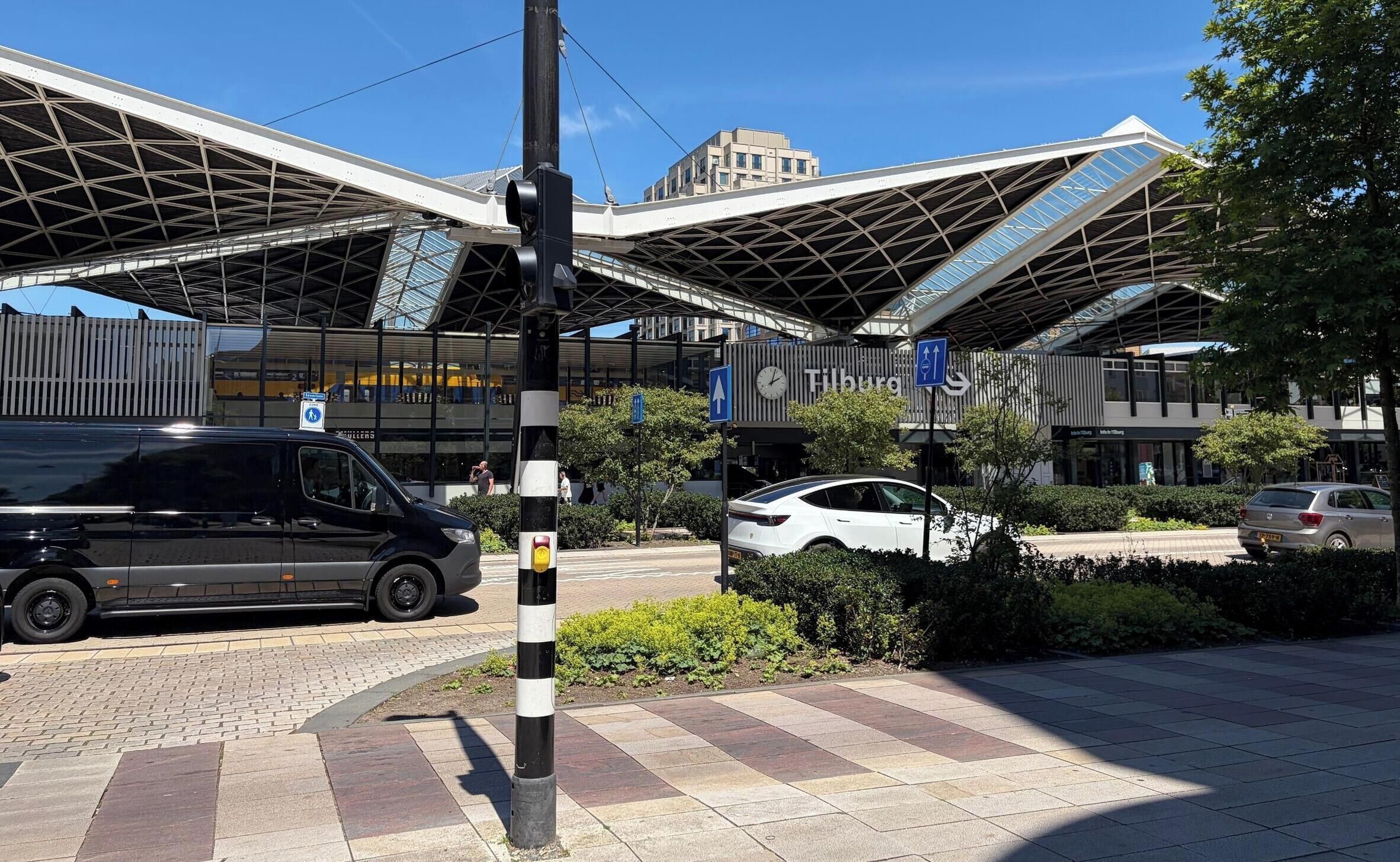 Un edificio moderno con una estructura de techo singular, un paso de peatones y un coche estacionado adelante.