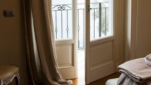 A room with a large window, a door, a bed, and a chair. - Perched above the gleaming waters of Lake Como (Riva)