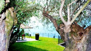 A patio area with a lawn, a black trash bin, and a metal fence. - Perched above the gleaming waters of Lake Como (Riva)