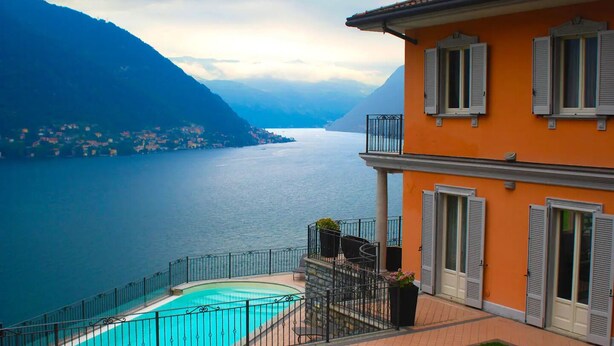 A building with a pool, a balcony, and a view of a lake and mountains. - Perched above the gleaming waters of Lake Como (Riva)