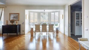 A spacious dining area with a wooden floor, a glass-top table, and white chairs. - Perched above the gleaming waters of Lake Como (Riva)