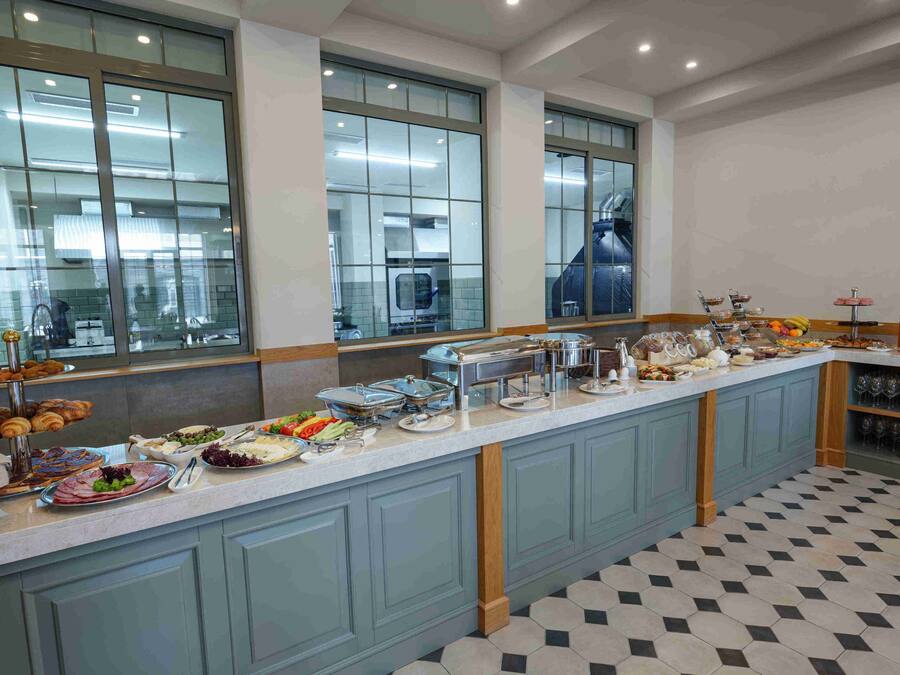 A buffet setup with various food items and a kitchen in the background.